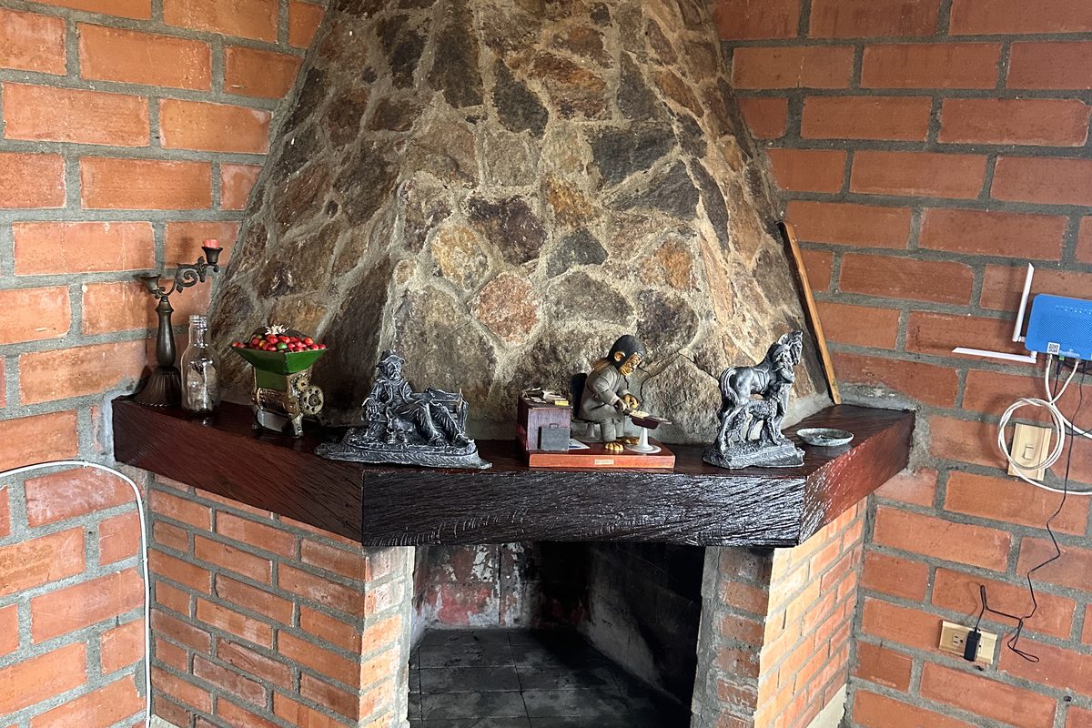 Chimenea de campana en piedra sobre muros de ladrillo, con repisa de madera y leña lista