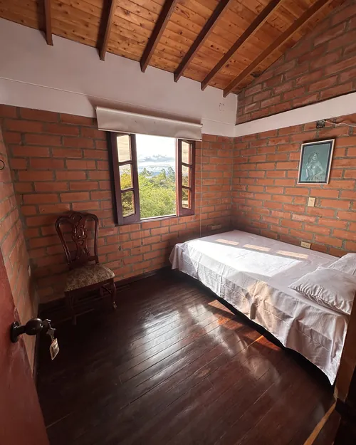 Habitación con dos camas sencillas, muros de ladrillo a la vista y ventana al valle
