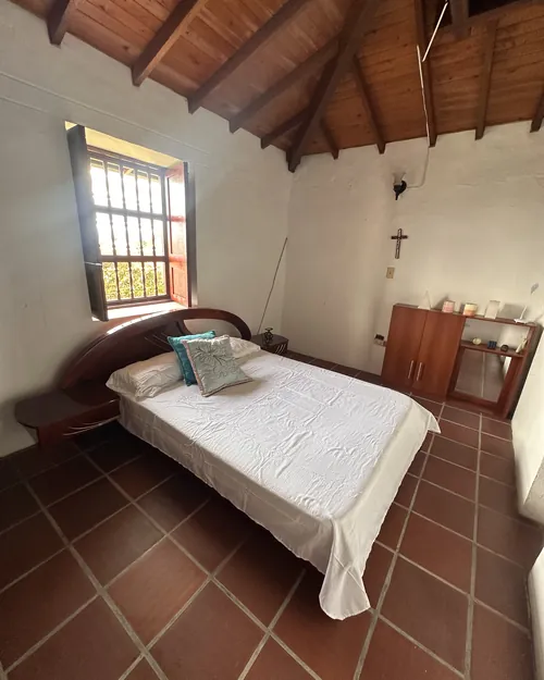 Habitación principal de La Amalita con cama doble, cabecero curvo de madera y ventana al jardín