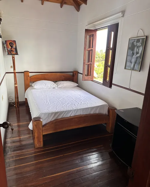 Habitación con cama doble de madera junto a un ventanal que da al campo